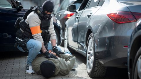 Der Fahrer des angehaltenen Autos liegt auf dem Bauch auf dem Boden. Seine Arme sind hinterm Rücken verschränkt. Ein Beamter kniet neben ihm und hält die Arme fest.