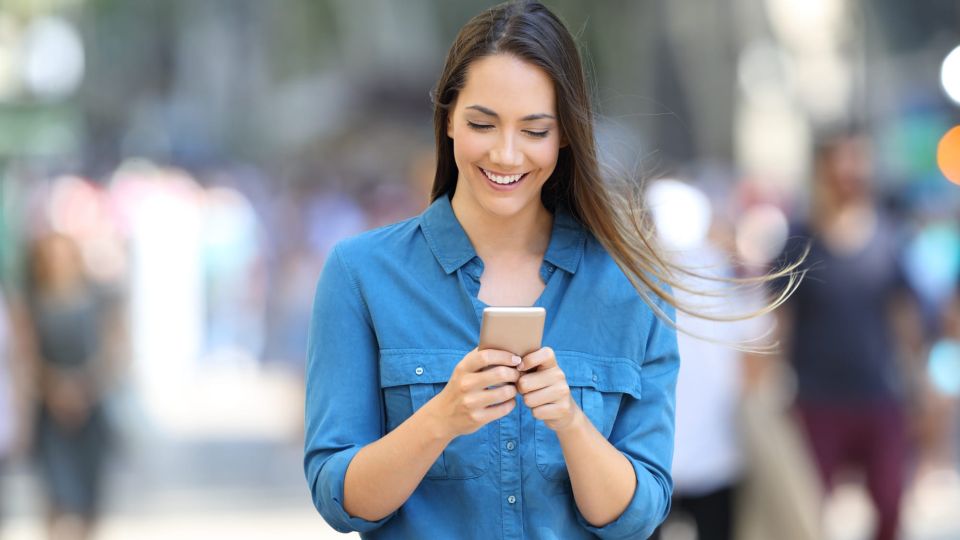 Eine Frau auf einer belebten Straße schaut lächelnd auf ihr Smartphone